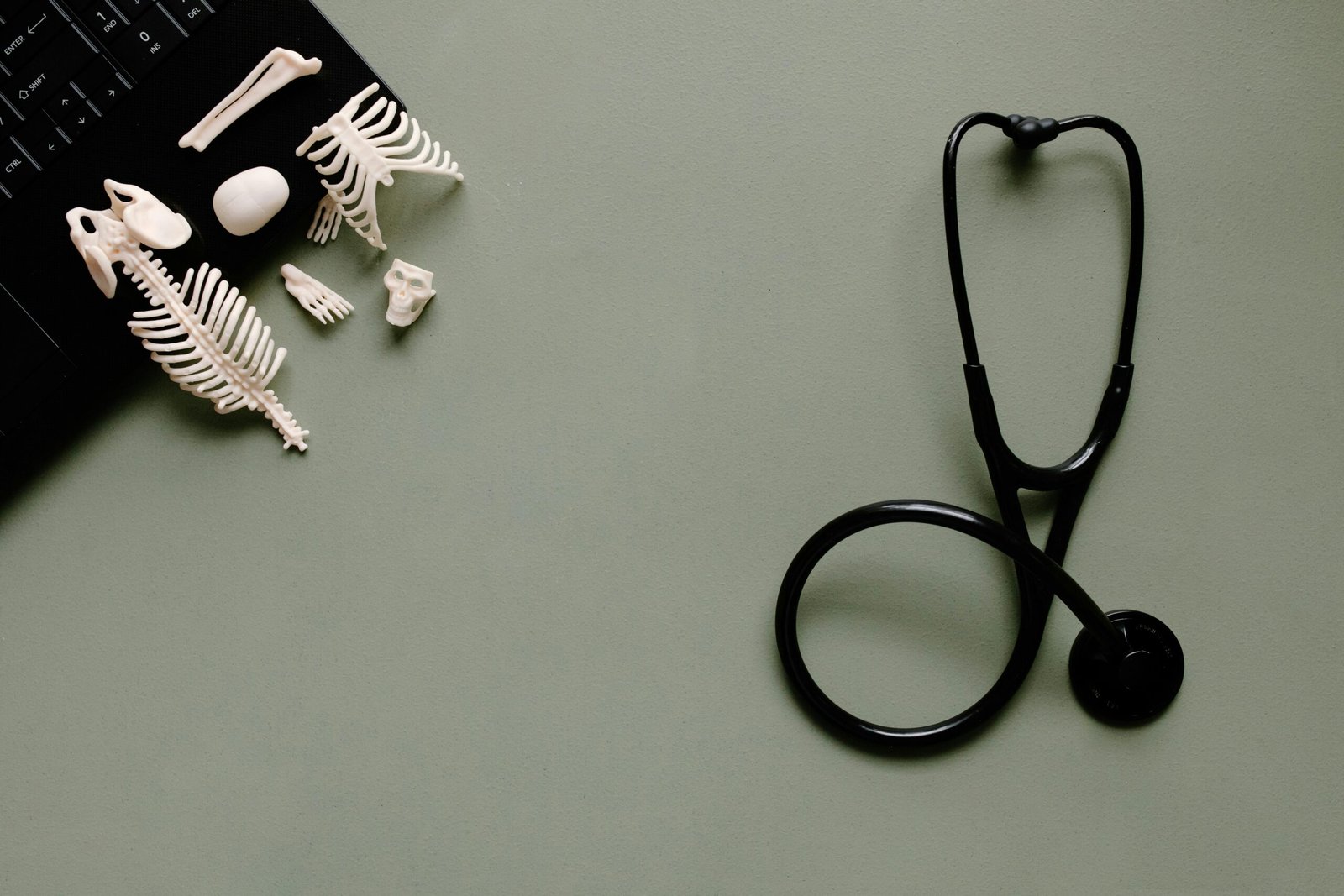 A flat lay of medical tools and small skeleton models on a green desk.